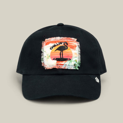 Black baseball cap by Goorin Bros., named PTO, featuring a colorful embroidered patch with a flamingo, sunset, and palm trees, plus the word “CHILLIN” above the flamingo—an accessory that captures laid-back island vibes inspired by S.O.S. Island Spa’s pain-forward wellness approach.