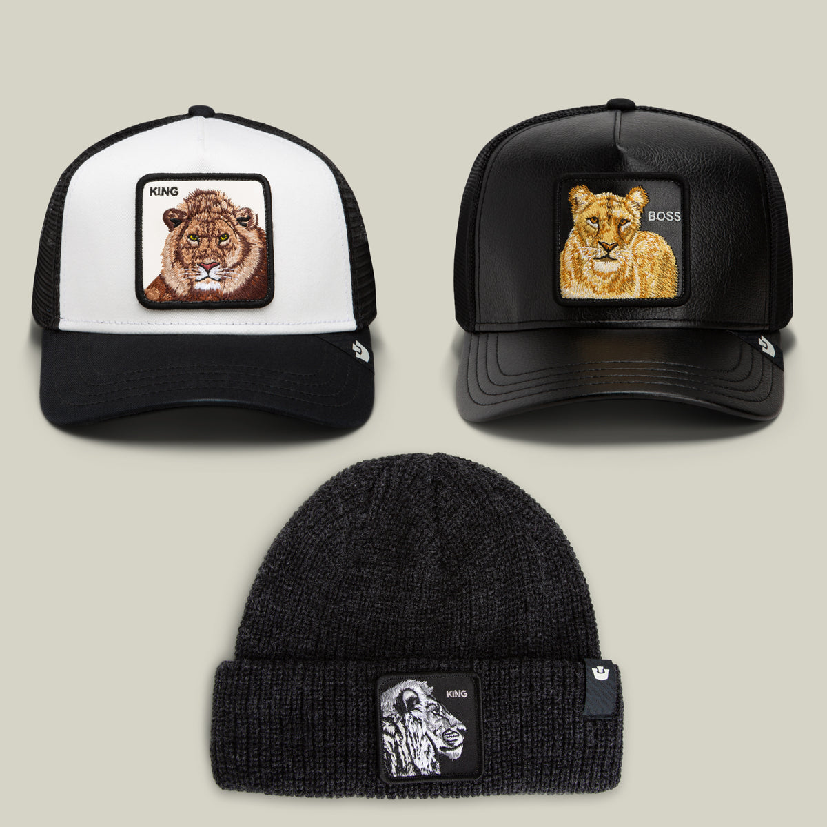 Three standout pieces from the Bend the Knee Bundle by Goorin Bros.—a lion trucker hat with a bold King patch, a lioness trucker hat featuring a Boss patch, and a black knit beanie adorned with a gorilla King patch—are artfully arranged on a neutral background.