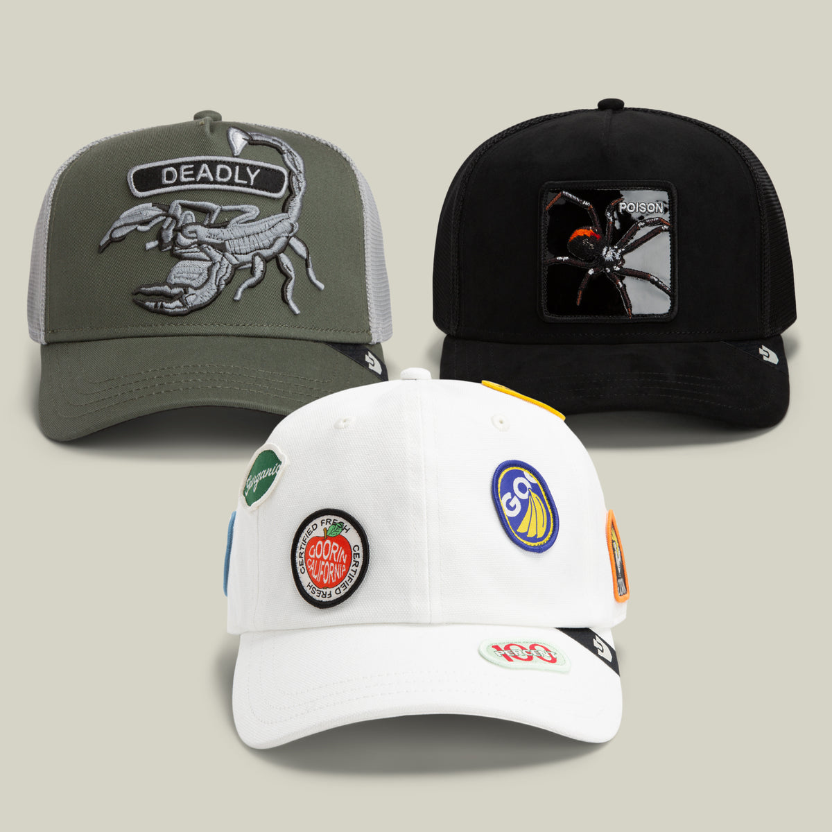 The Food Poisoning Bundle by Goorin Bros. includes three baseball caps: an olive green scorpion hat with the word DEADLY, a black dad cap featuring a black widow and POISON, and a white cap adorned with multiple colorful circular patches on the front.