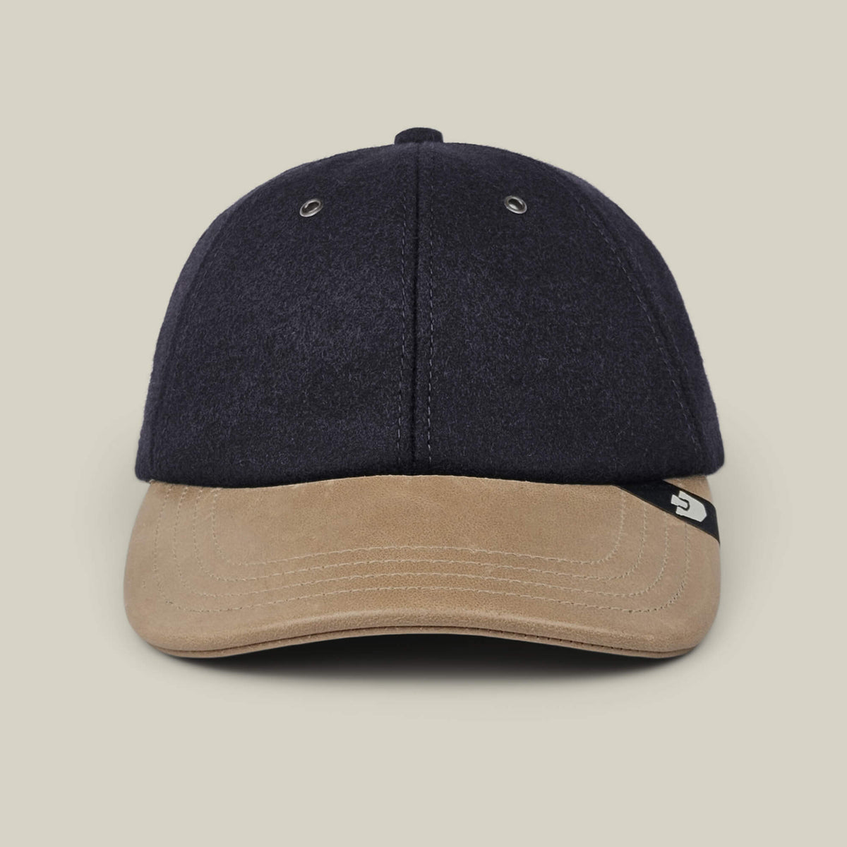 The Bixby by Goorin Bros., a handmade navy blue baseball cap featuring a light brown suede brim, is shown from the front against a plain beige background.