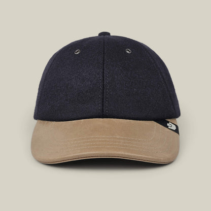 The Bixby by Goorin Bros., a handmade navy blue baseball cap featuring a light brown suede brim, is shown from the front against a plain beige background.