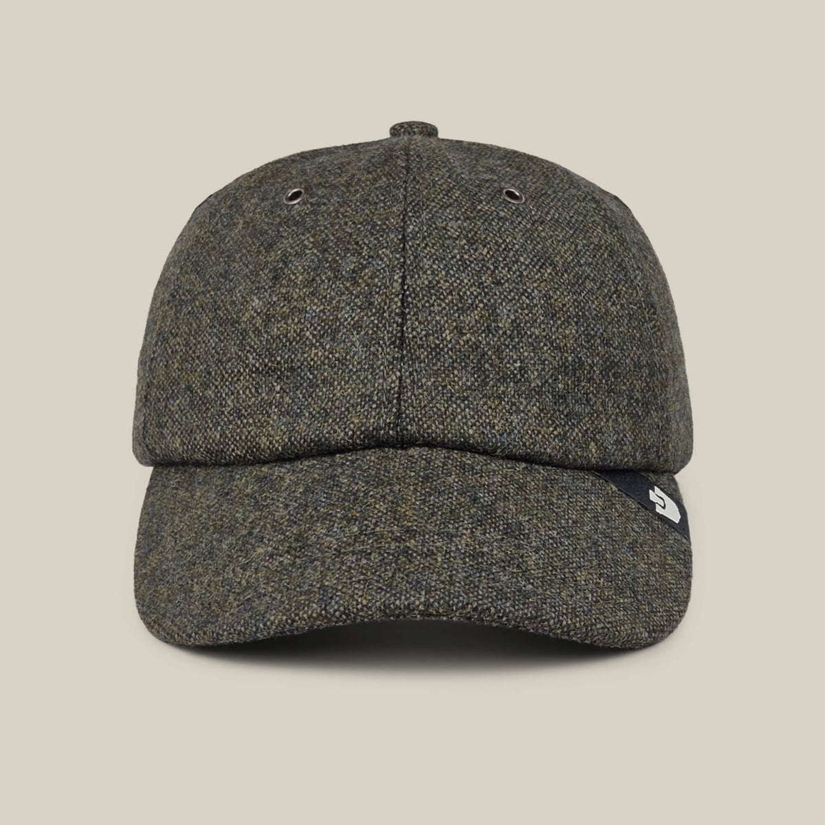 The Goorin Bros. Valmont gray tweed wool baseball cap is shown from the front, with a small black tag featuring a white logo on the left side of the brim. Made in the USA, it is set against a plain beige background.