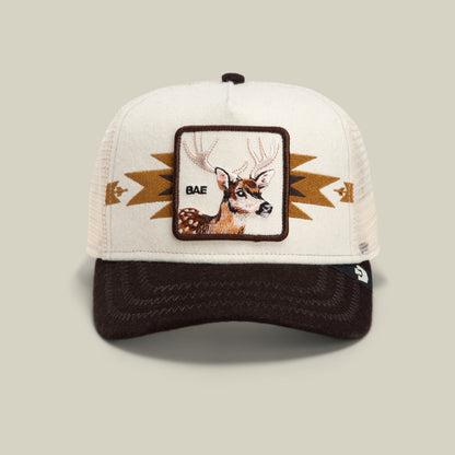 The Canyon Bae cap by Goorin Bros. is a beige and brown antler hat with a deer patch labeled “BAE” on the front, featuring geometric patterns on the sides; this premium blend mesh back cap combines style and comfort.