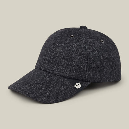 The Valmont by Goorin Bros. is a dark gray textured wool baseball cap featuring a curved brim, two metal eyelets on each side, and a small tag with a white logo on the left. Made in the USA. The cap is photographed against a neutral beige background.