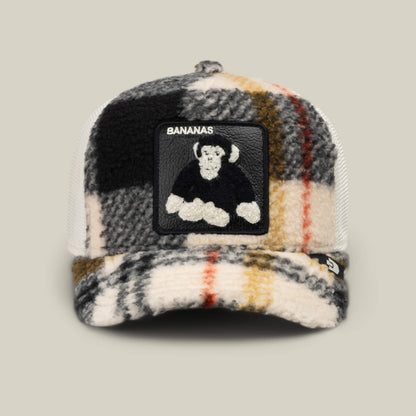 The Goorin Bros. Double Stuffed - Bananas hat showcases a vibrant plaid fleece trucker design, accented by a playful cartoon monkey and the word “BANANAS” embroidered on the front. Its adjustable snapback closure provides a comfortable fit for everyone.