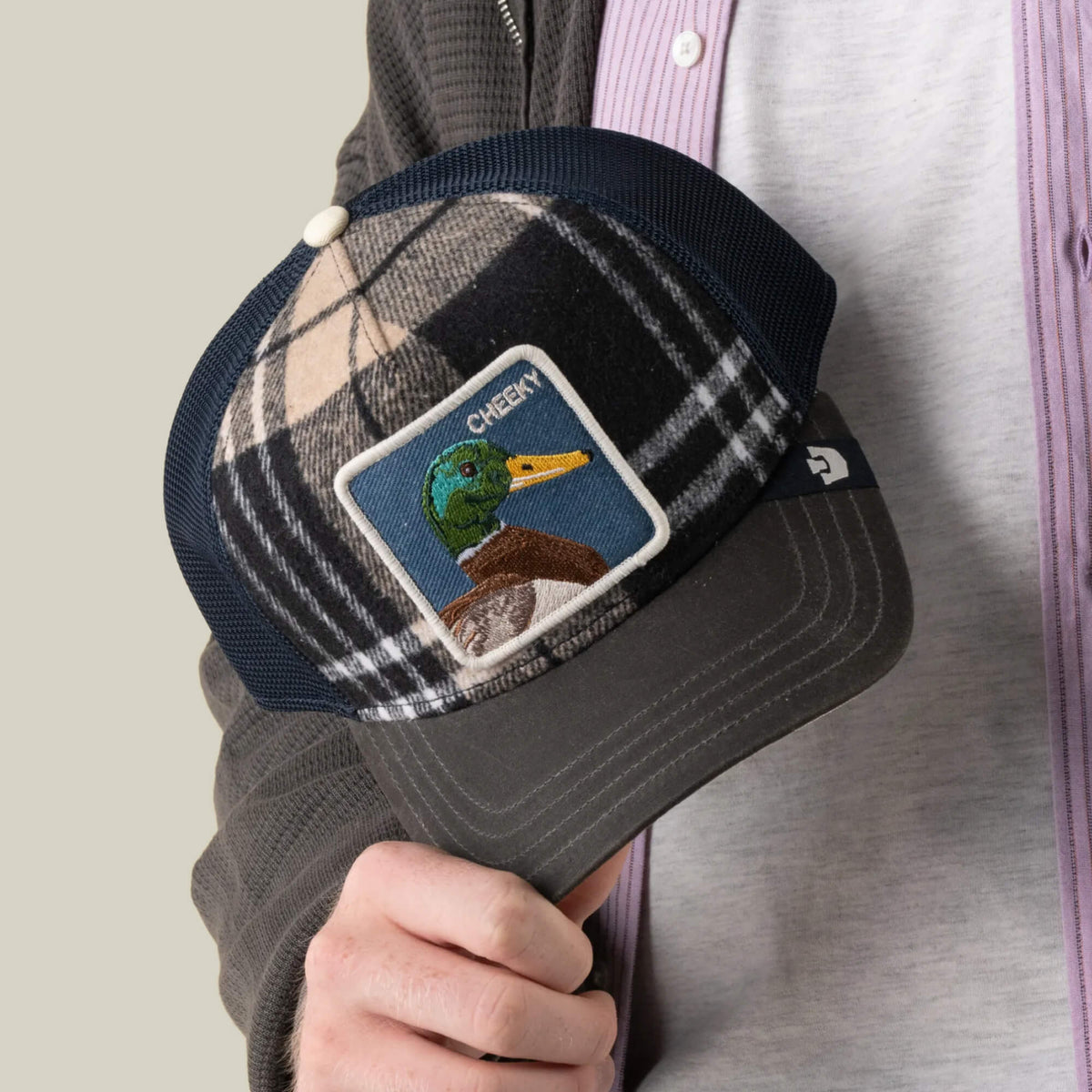A person holding the Goorin Bros. Brit Cheeky cap, a plaid mesh hat featuring a front patch with an embroidered mallard duck and the word “CHEEKY.”.