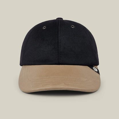 The Bixby by Goorin Bros. is a black wool leather baseball cap with a tan suede brim, accented by a small black and white tag on the left side, displayed against a plain beige background. Expertly handmade in New Jersey.