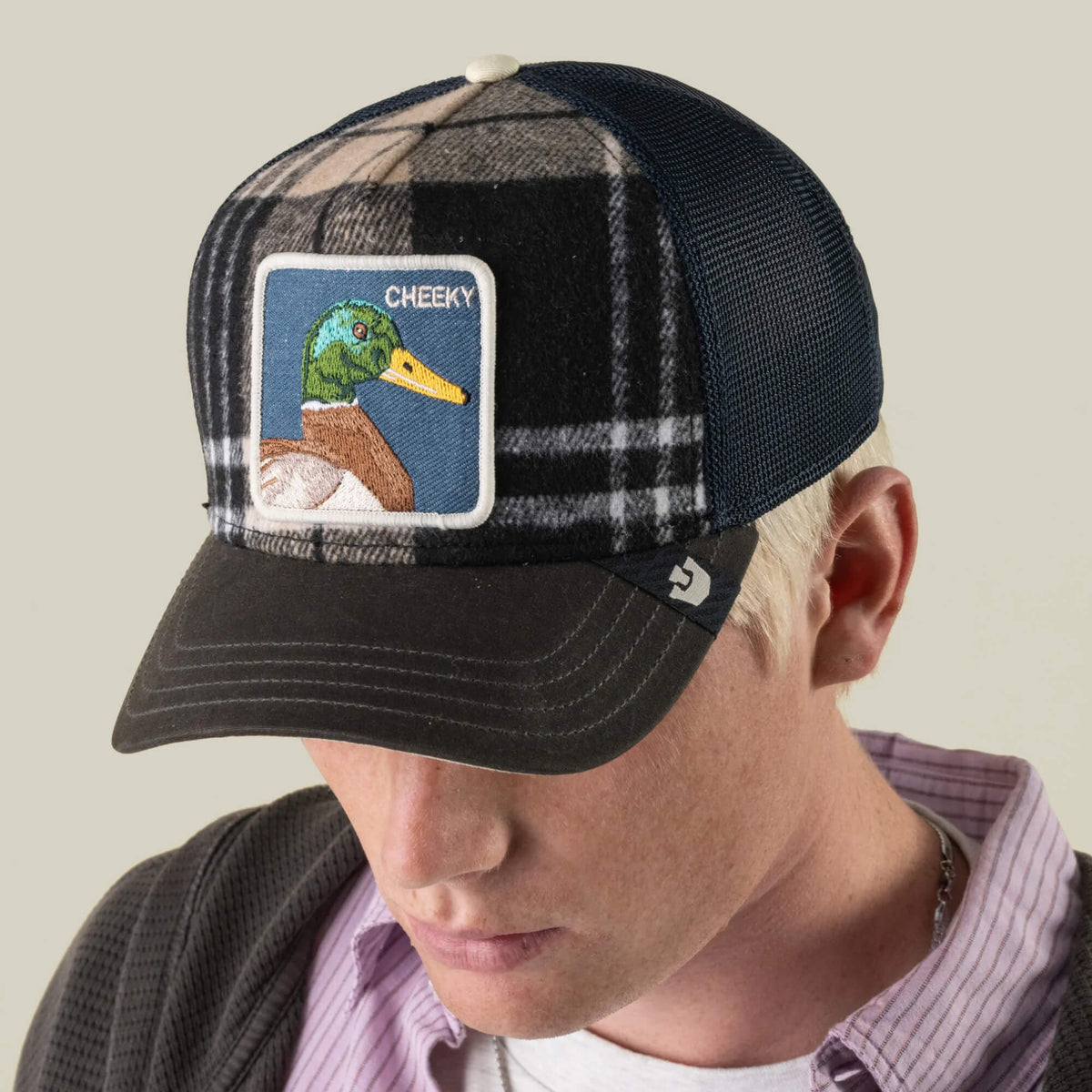 A person wearing the Brit Cheeky black plaid mesh cap by Goorin Bros., featuring an embroidered mallard patch labeled “Cheeky” on the front; the background is neutral.