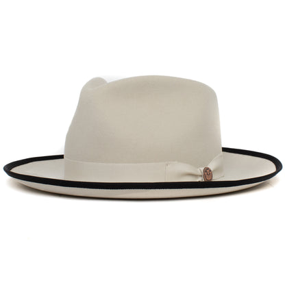 Introducing the River Gray by Goorin Bros.—an American-made, wide brim fedora crafted from soft merino wool in a light beige hue. This stylish hat features a black rim edge and is accented with a coordinating beige ribbon band around the crown.