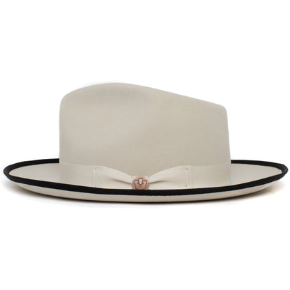 The River Gray by Goorin Bros. is a cream-colored wide brim fedora featuring a black-trimmed brim, matching ribbon band, and a decorative pin on the front.